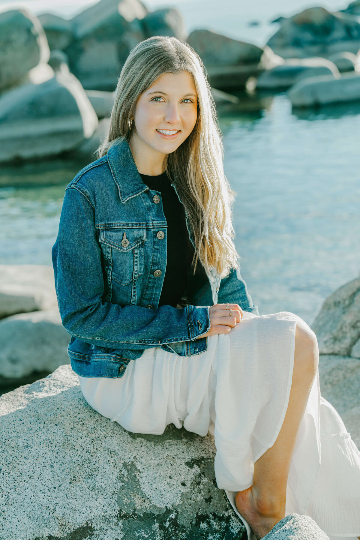 senior girl portrait session at speedboat beach sitting on a boulder looking at camera wearing a jean jacket photographed by annie X photographie