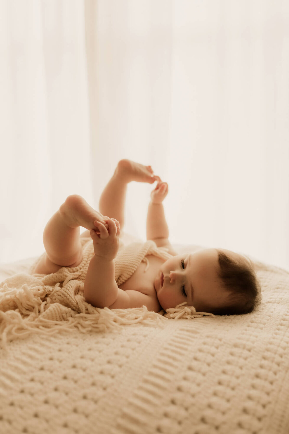 Baby girl holds her feet while laying down for a studio portrait in Oklahoma City.