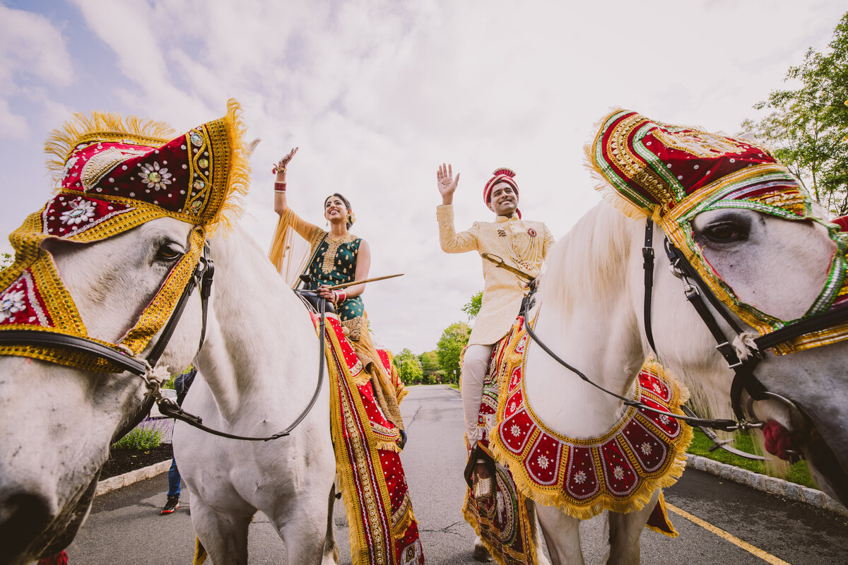 An indian bride and groom on their own horses dancing during the baraat on their wedding day