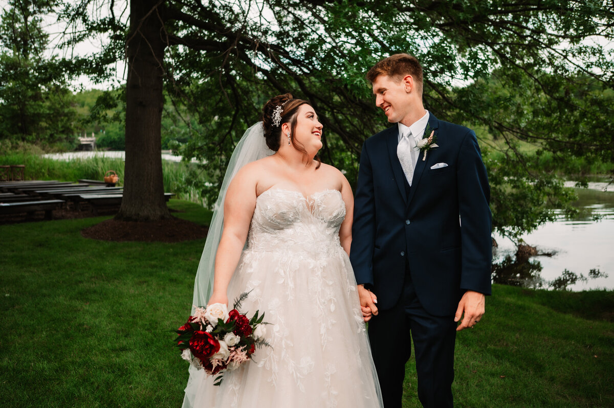 NEwlyweds smile at each other while walking under a tree holding hands