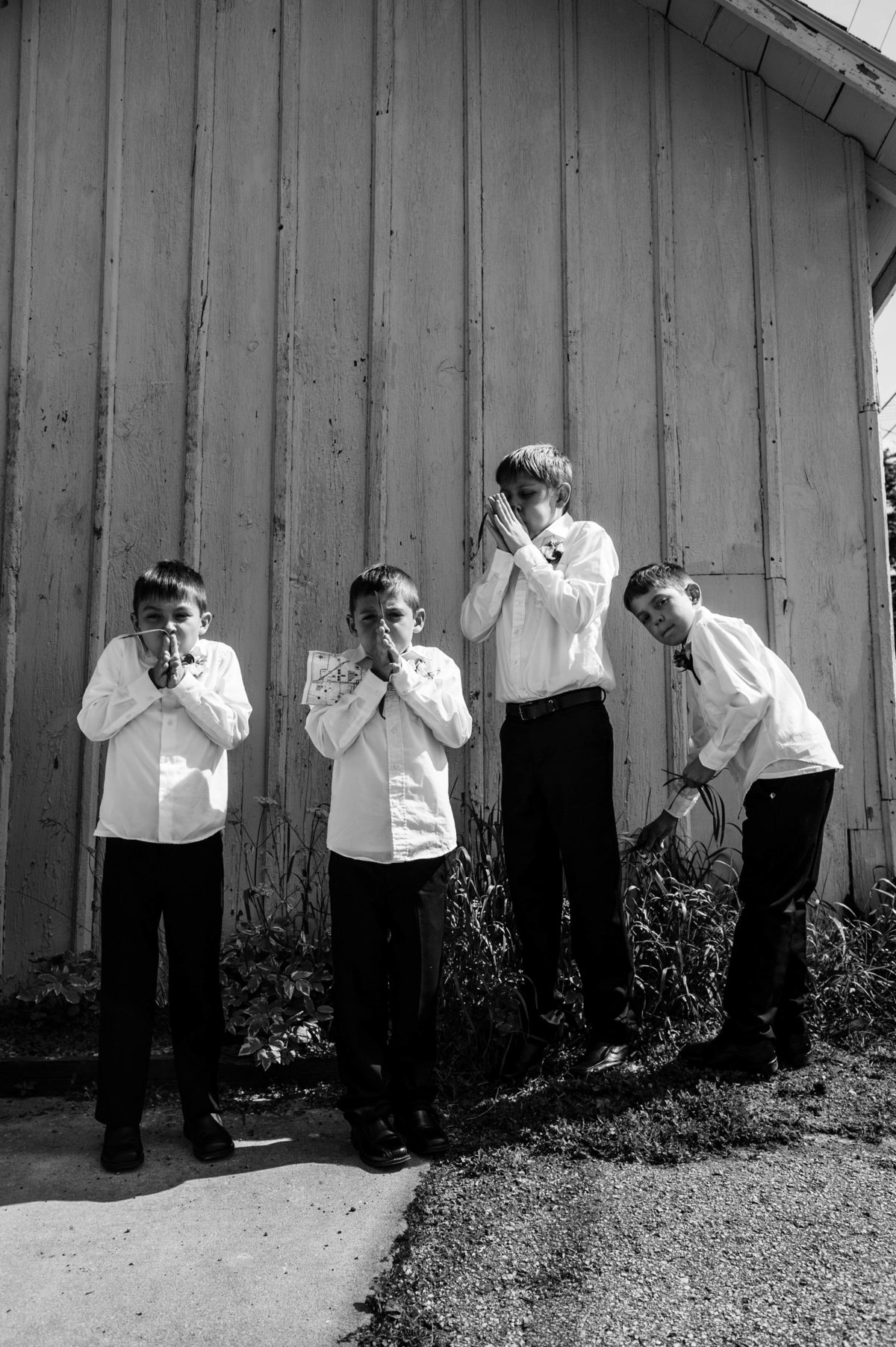 four boys blowing grass blades behind church after wedding