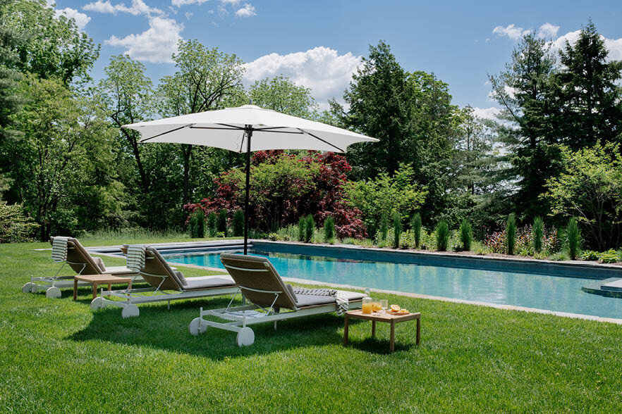 Another angle of the Concord estate pool, highlighting modern chaise lounges from Design Within Reach and a Tucci umbrella, perfect for luxury outdoor relaxation.