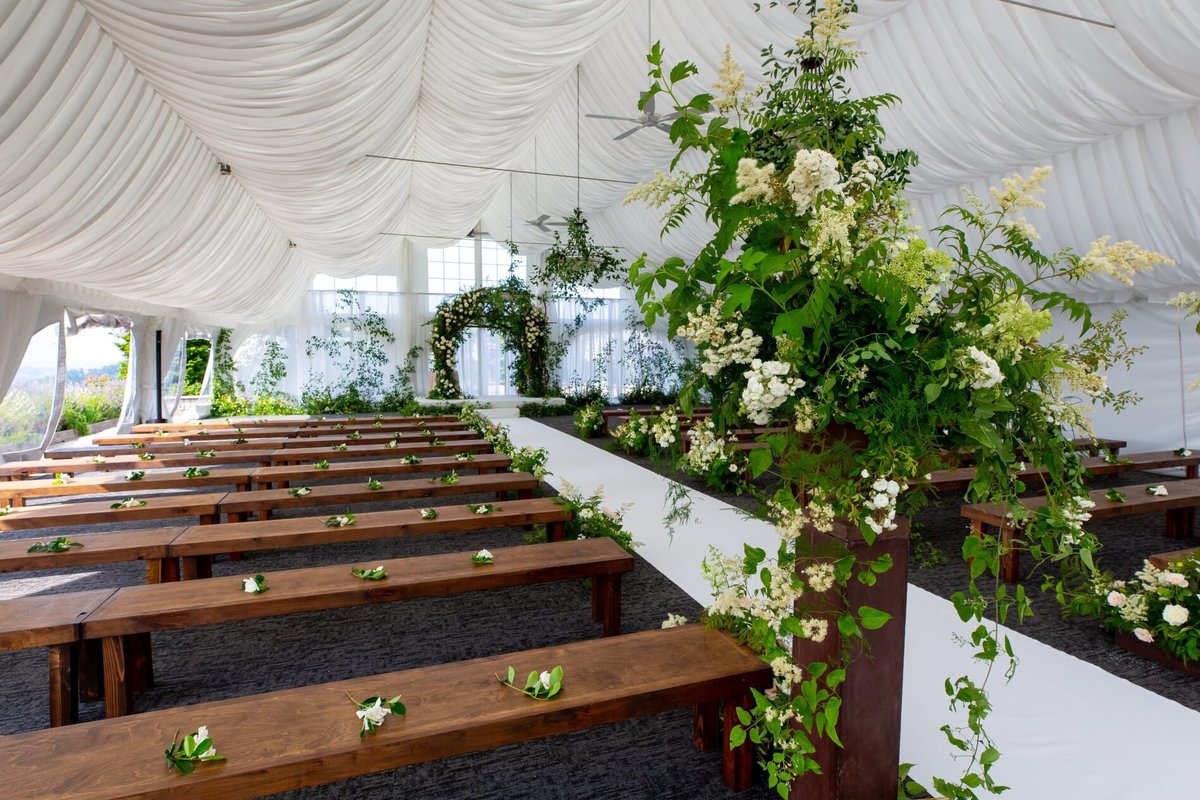 Wedding ceremony with wooden benches and green and white floral decor at Newcastle tent