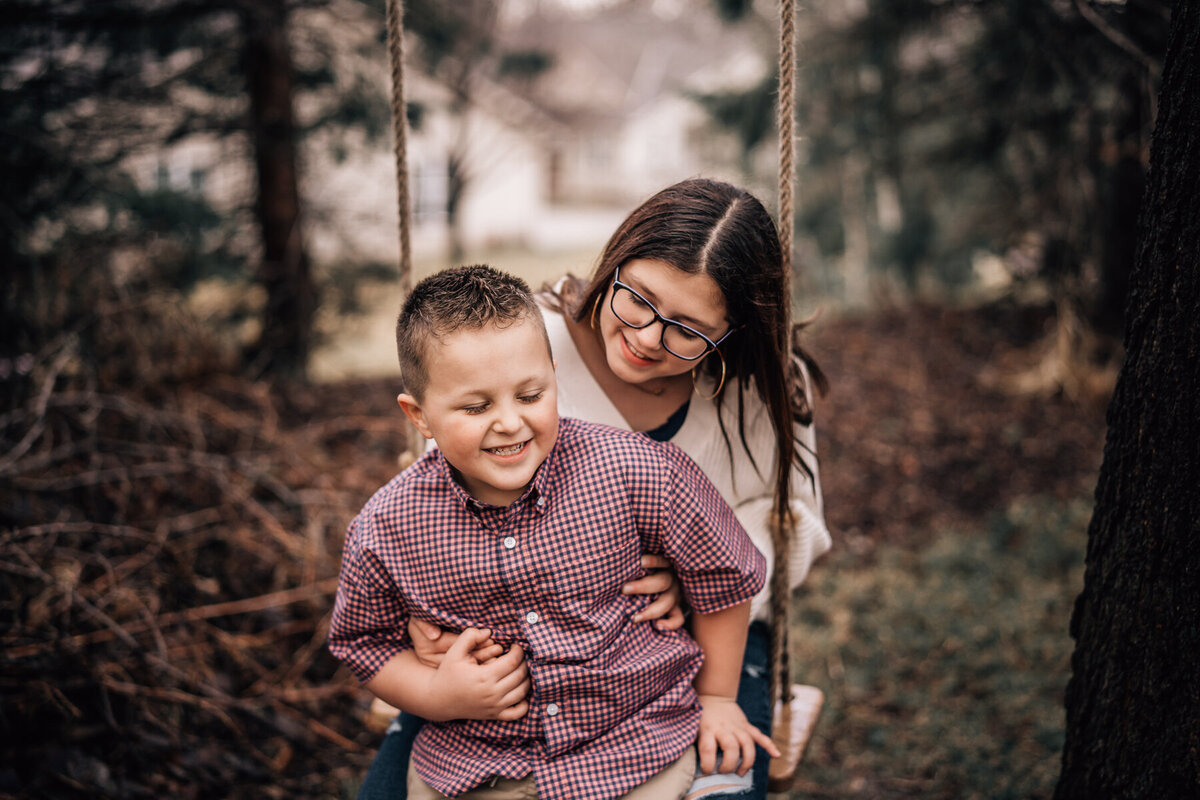 Two siblings hug on a swing in their Minnesota backyard. while being photographed by Minneapolis family photographer, Kate Simpson