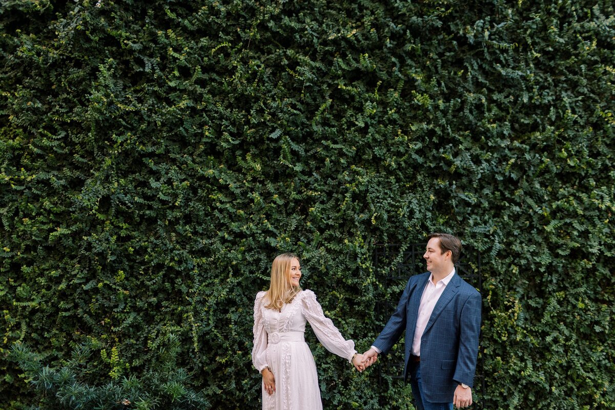 bride-to-be guides her fiance down a path in front of an ivy-covered wall