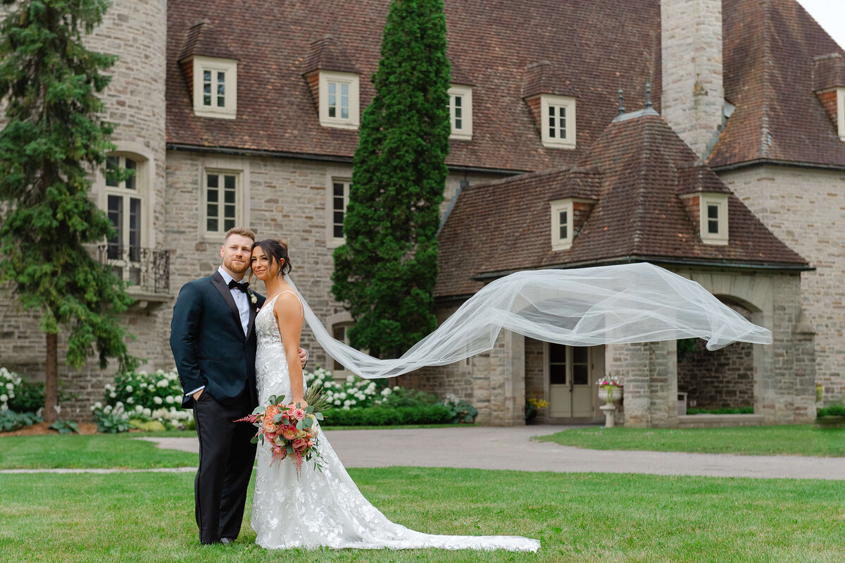 a photo of a bride and groom with the veil blowing in the wind taken outside Eaton Hall by Ottawa wedding photographer JEMMAN Photography