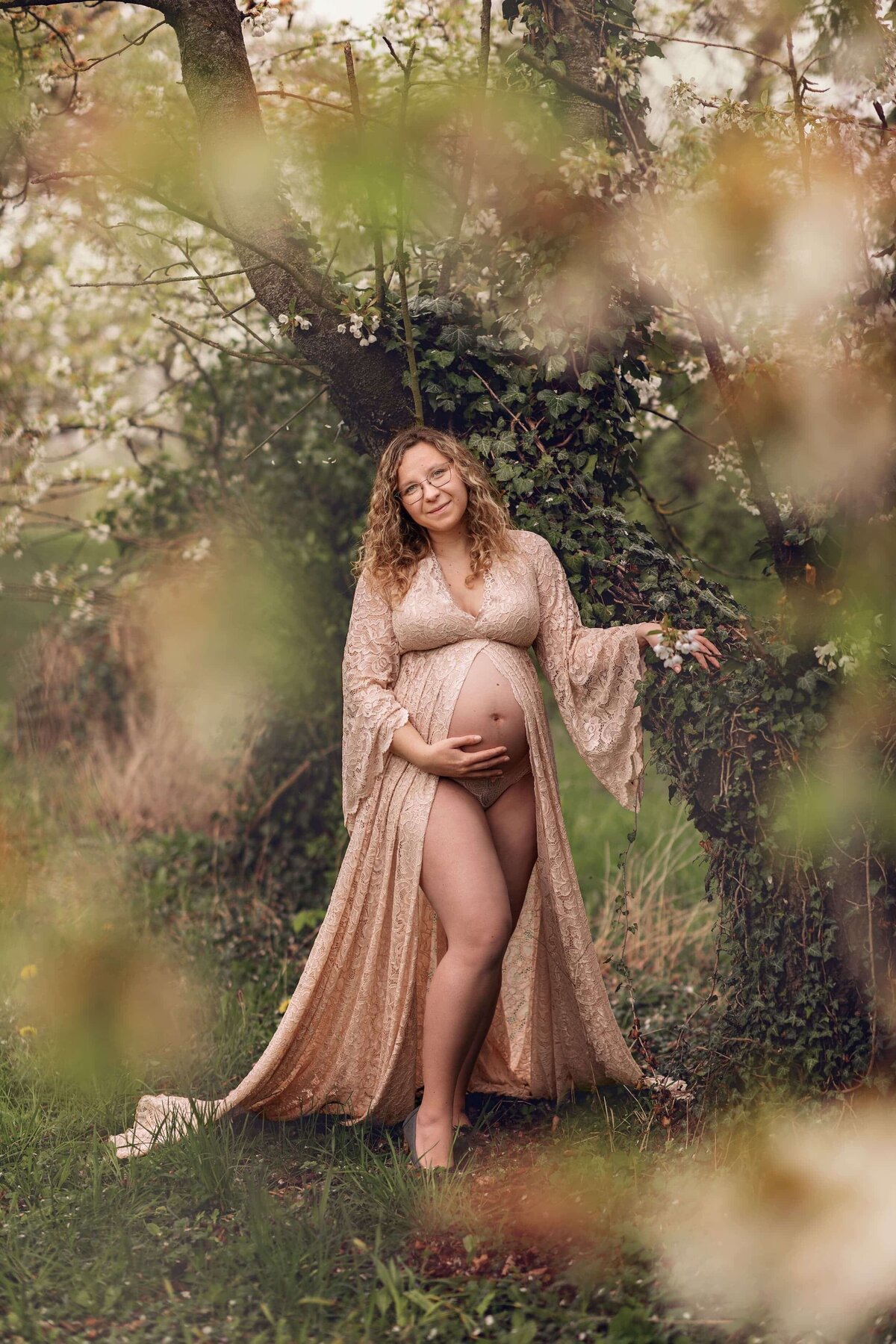 femme enceinte souriant portant robe de dentelle dehors au milieu des fleurs et feuilles au printemps