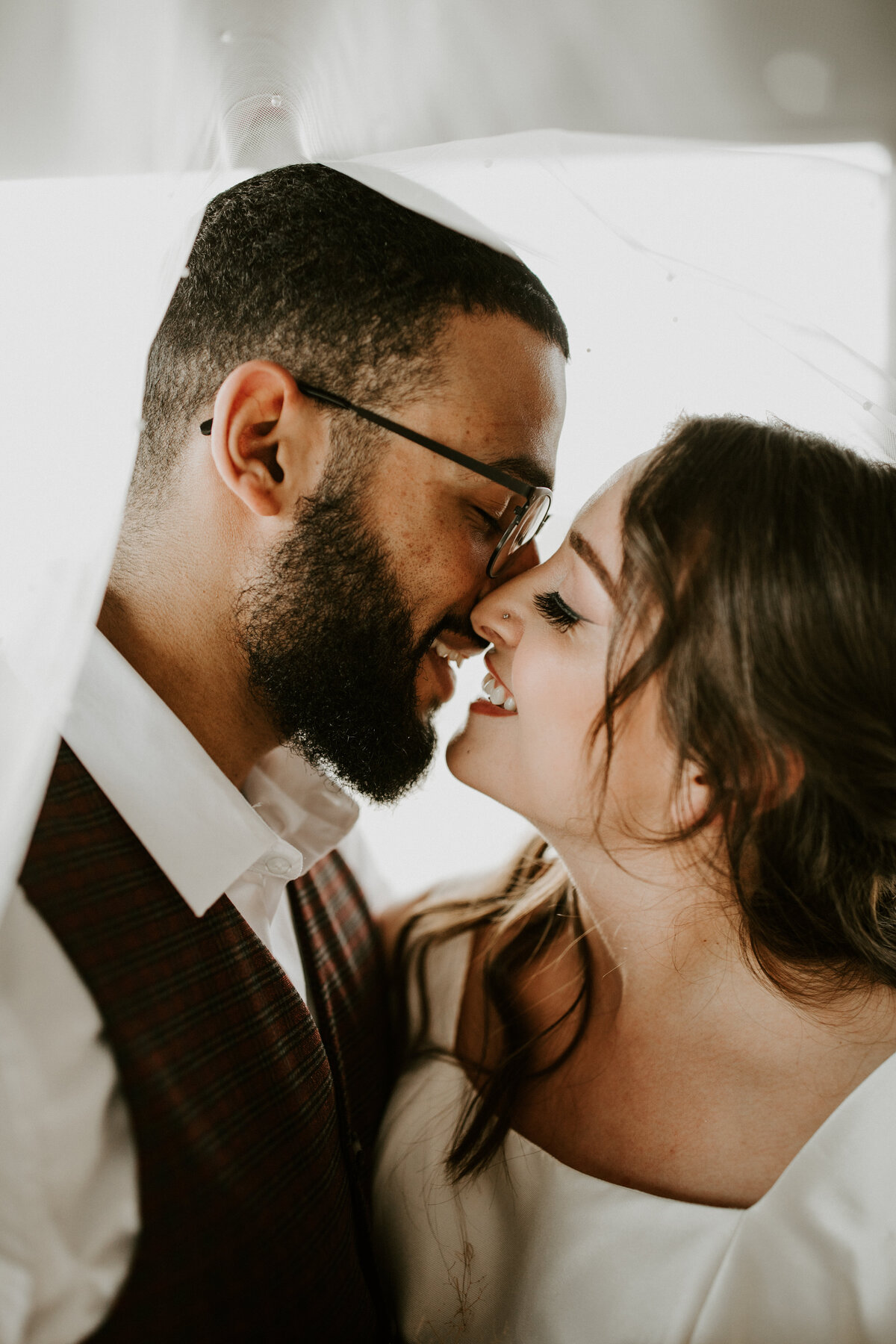 Bride and groom wearing white lean in for a kiss in bright and airy atmosphere.