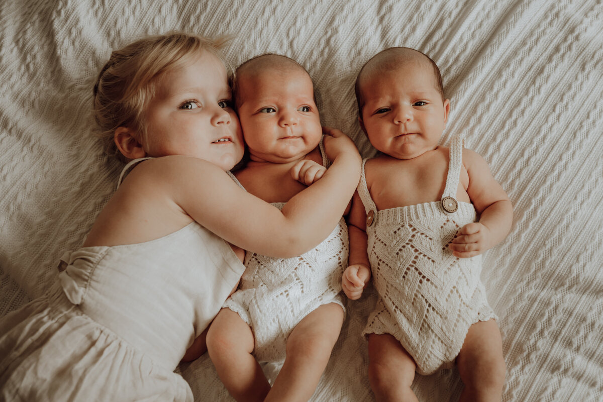 Zusje omhelst baby tweeling tijdens newborn fotoshoot in boho setting