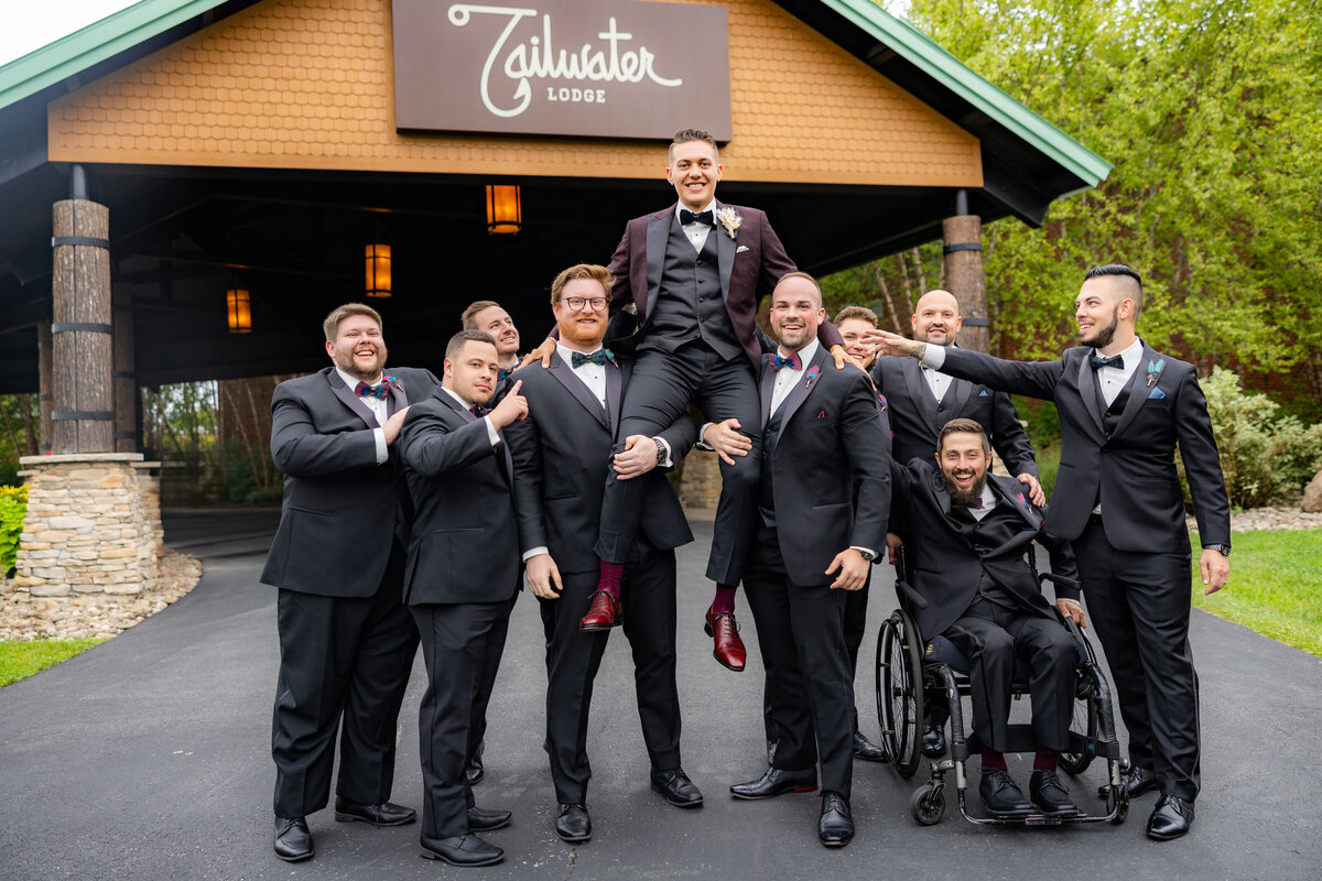 Groom is carried by groomsmen in front of a Tailwater Lodge, their wedding venue in upstate new york. Photo by wedding photographer from Sacramento, CA, Philippe Studio Pro.