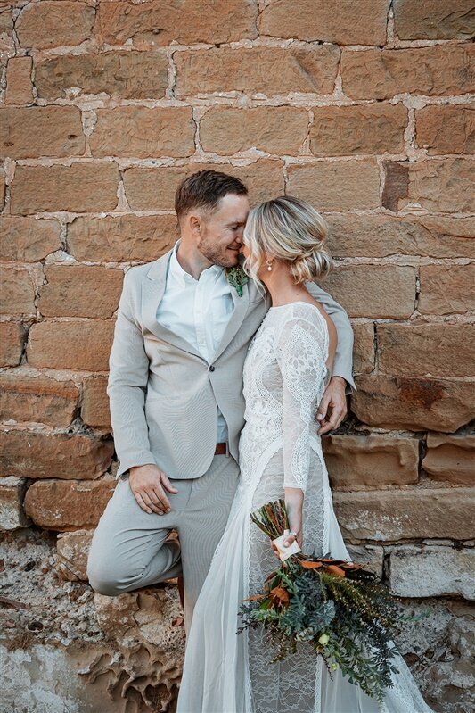 Indulge in the timeless beauty of Maddi and Jeremy as they share a captivating moment, gazing into each other's eyes while leaning against a rustic wall.