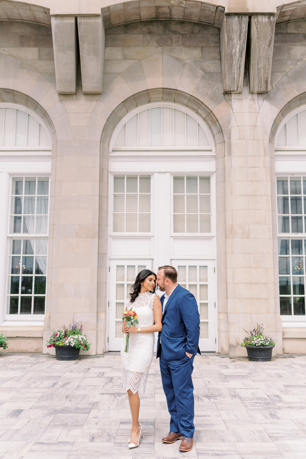Elopement wedding inspiration, gorgeous trendy couple standing in front of Fairmont Hotel Macdonald, bride wearing a stunning lace knee-length wedding dress.