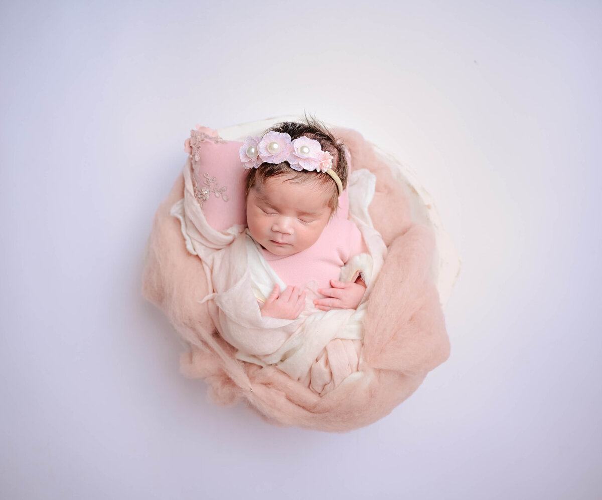 Newborn photo session in Bremerton, WA. Newborn dressed in pink, wrapped in pink and white fluffs, and posed sleeping in a white bowl. Image captured by Beth Benecki of E. Benecki Photography.