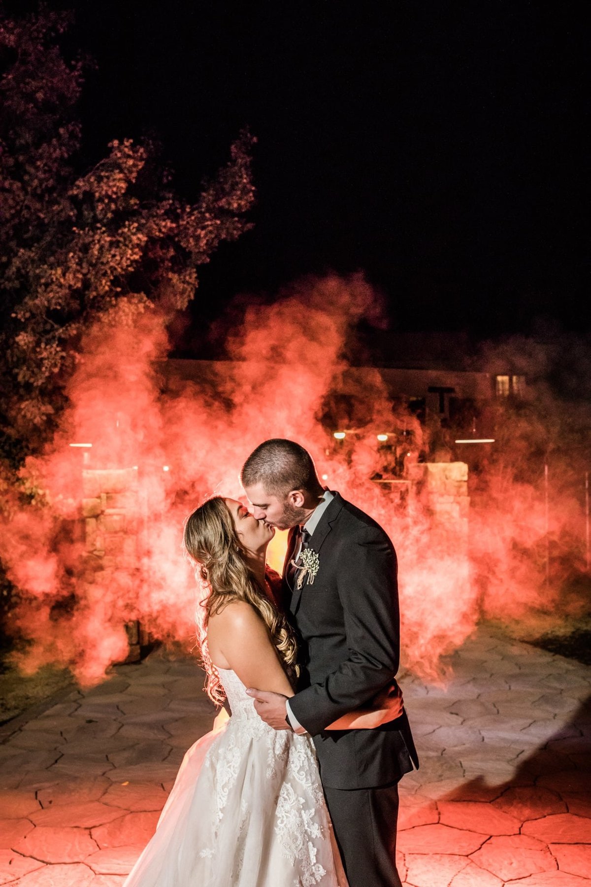 Bride and Groom share a romantic kiss with a red hue mist in the background