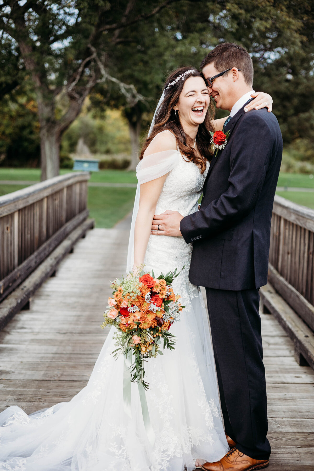 A bride and groom stand on a boardwalk bridge laughing and hugging captured by a Saratoga Springs wedding photographer