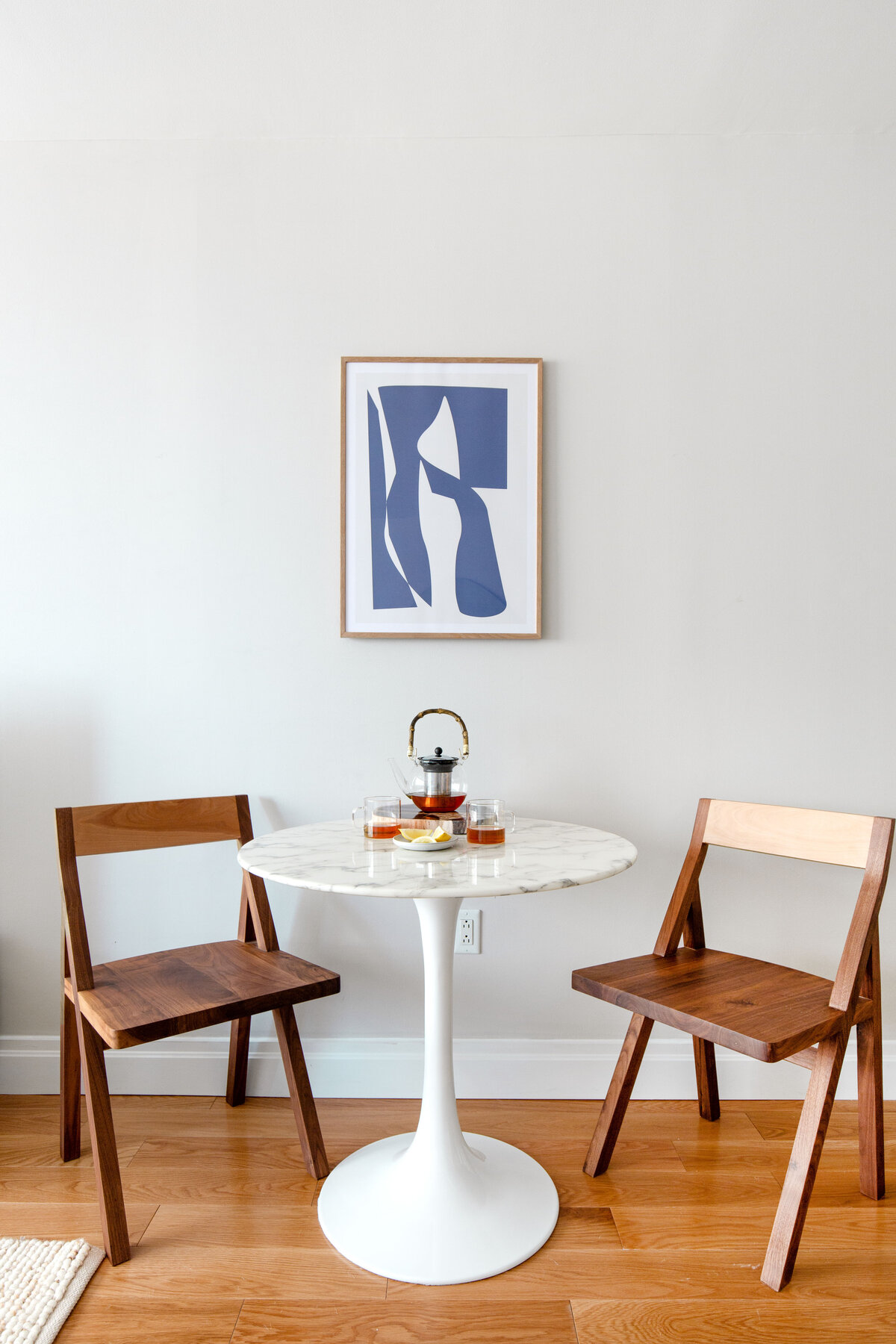 Small dining area with light grey painted walls, Saarinen tulip marble dining table, wooden dining chairs and blue abstract artwork on wall