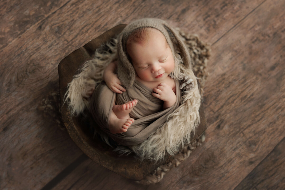 Newborn baby in a wooden bowl wearing a brown bunny bonnet at a newborn photography session at a leesburg va photo studio