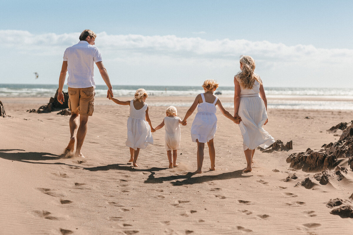 Family all dressed in white holding hands at the beach