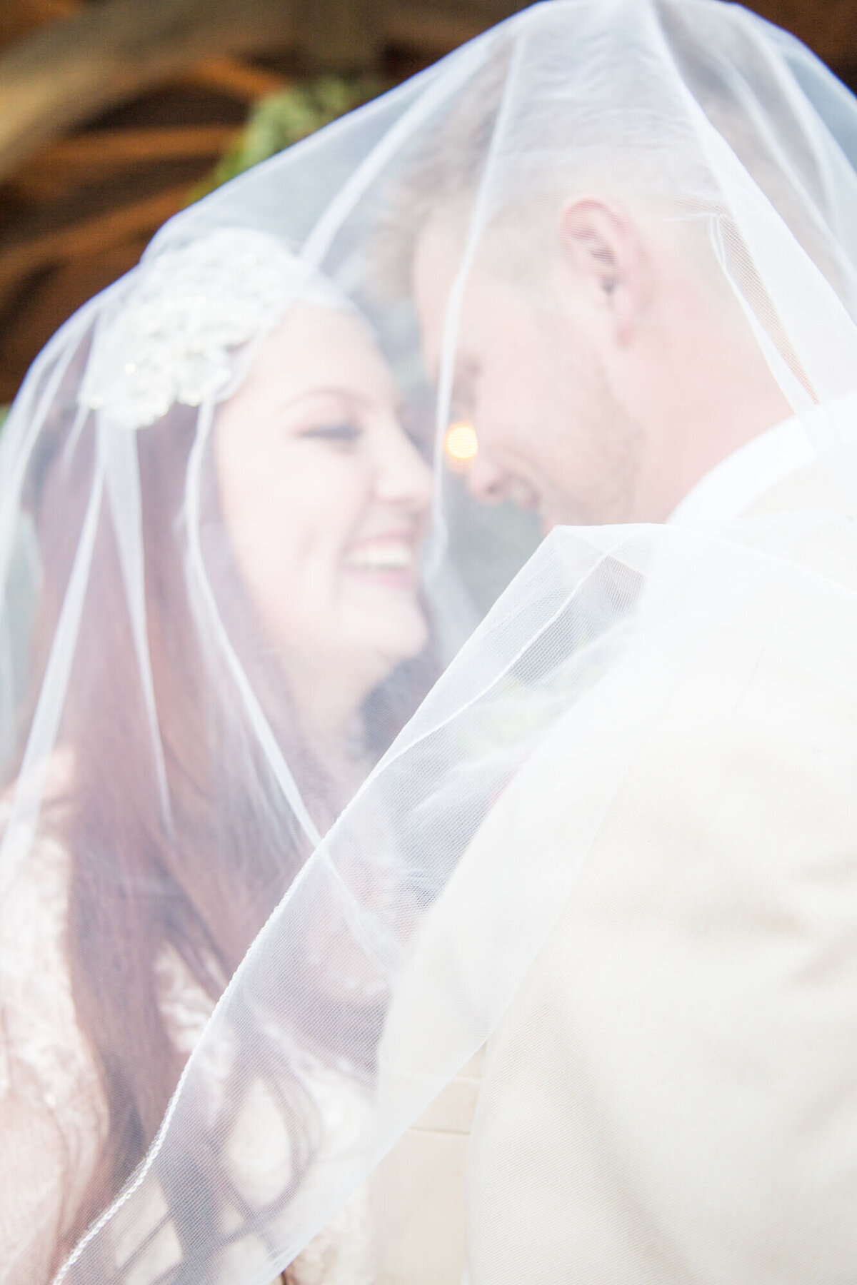 fine art portrait of redheaded bride and her groom smiling at each other under a veil