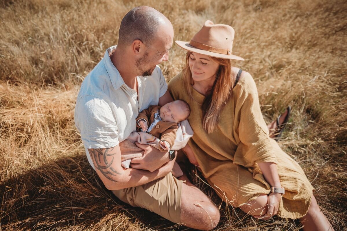 new parents with fresh baby sitting in the grass posing during their outdoor newborn photoshoot