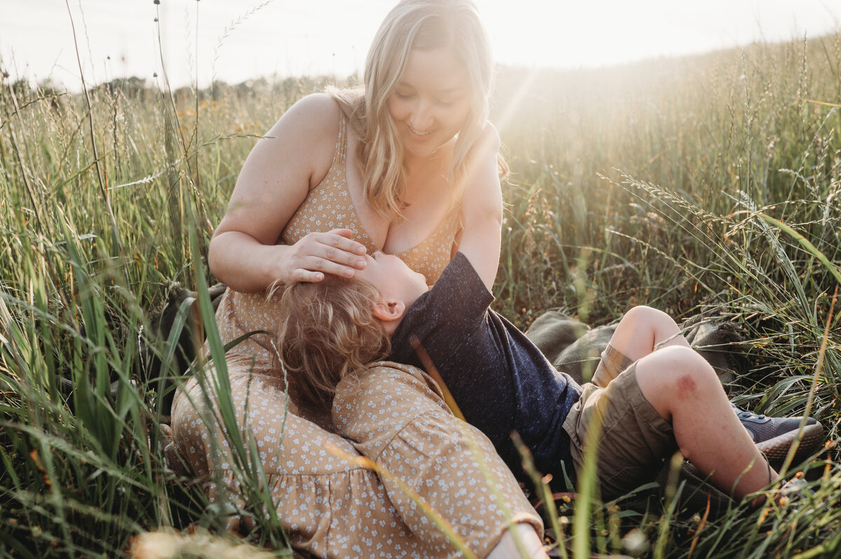 Mother holds young son in her lap in the open field at sunset