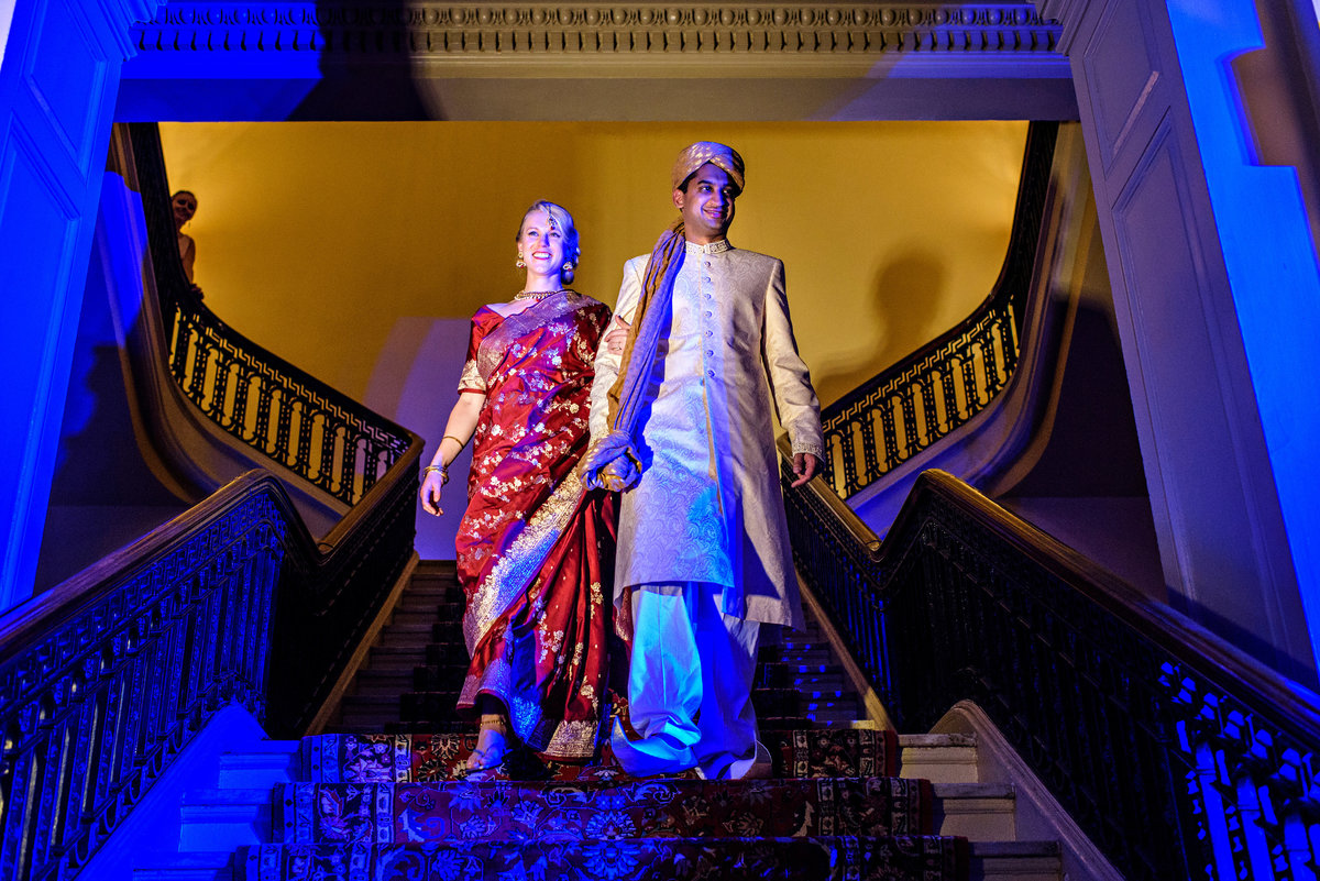 An indian wedding couple walk down the staircase to their reception at the Racquet Club of Philadelphia.