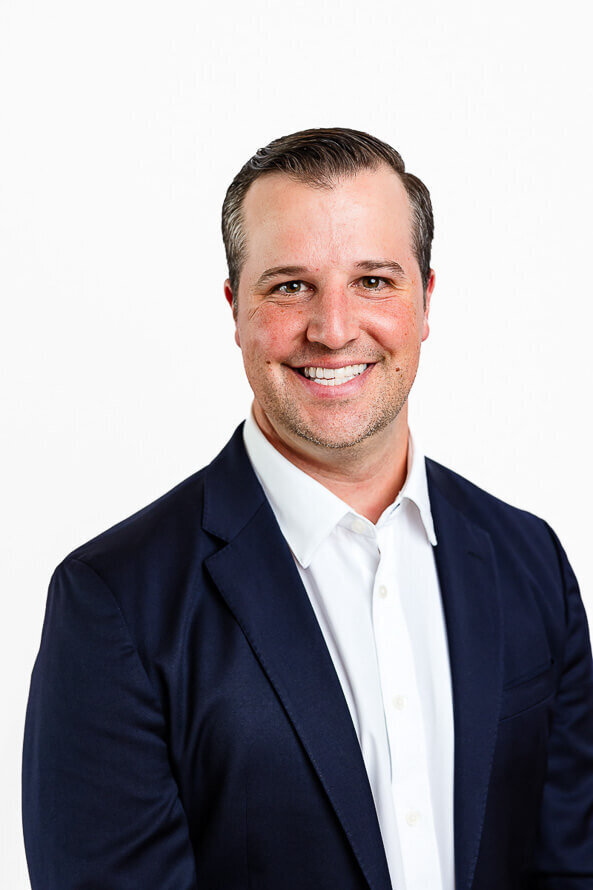 Close up headshot of man in blue jacket on a white backdrop.