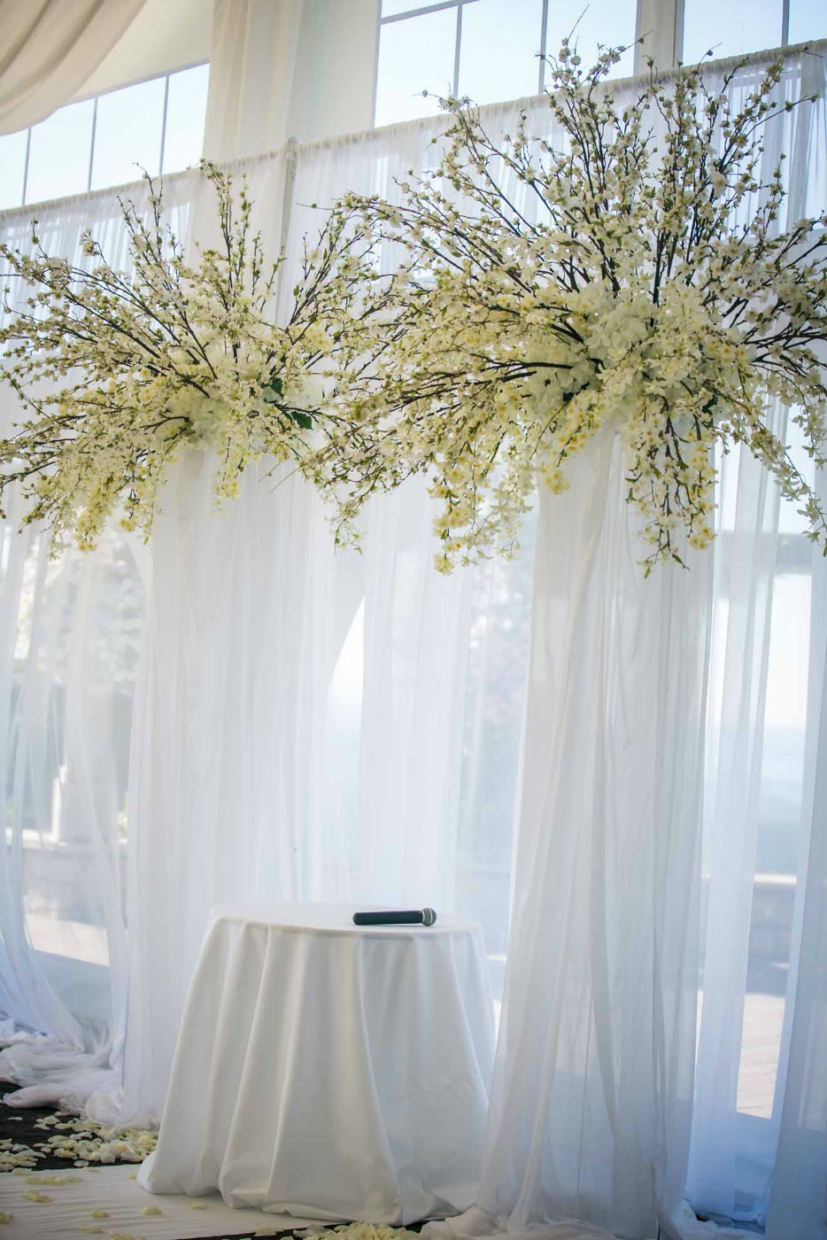 tall white wedding arch with draped pillars, cherry blossom and white orchids