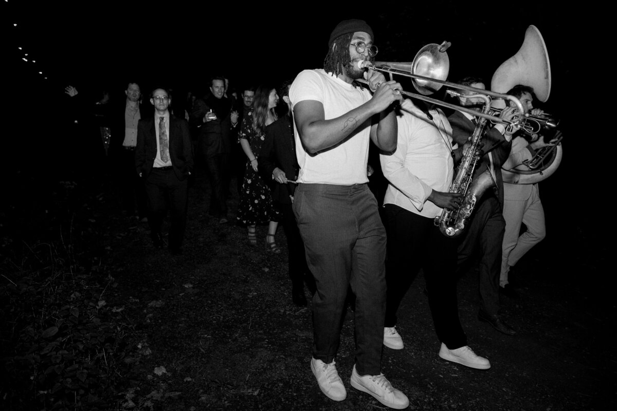 Black and white photo of musicians playing in front of wedding guests with twinkle lights in the background.