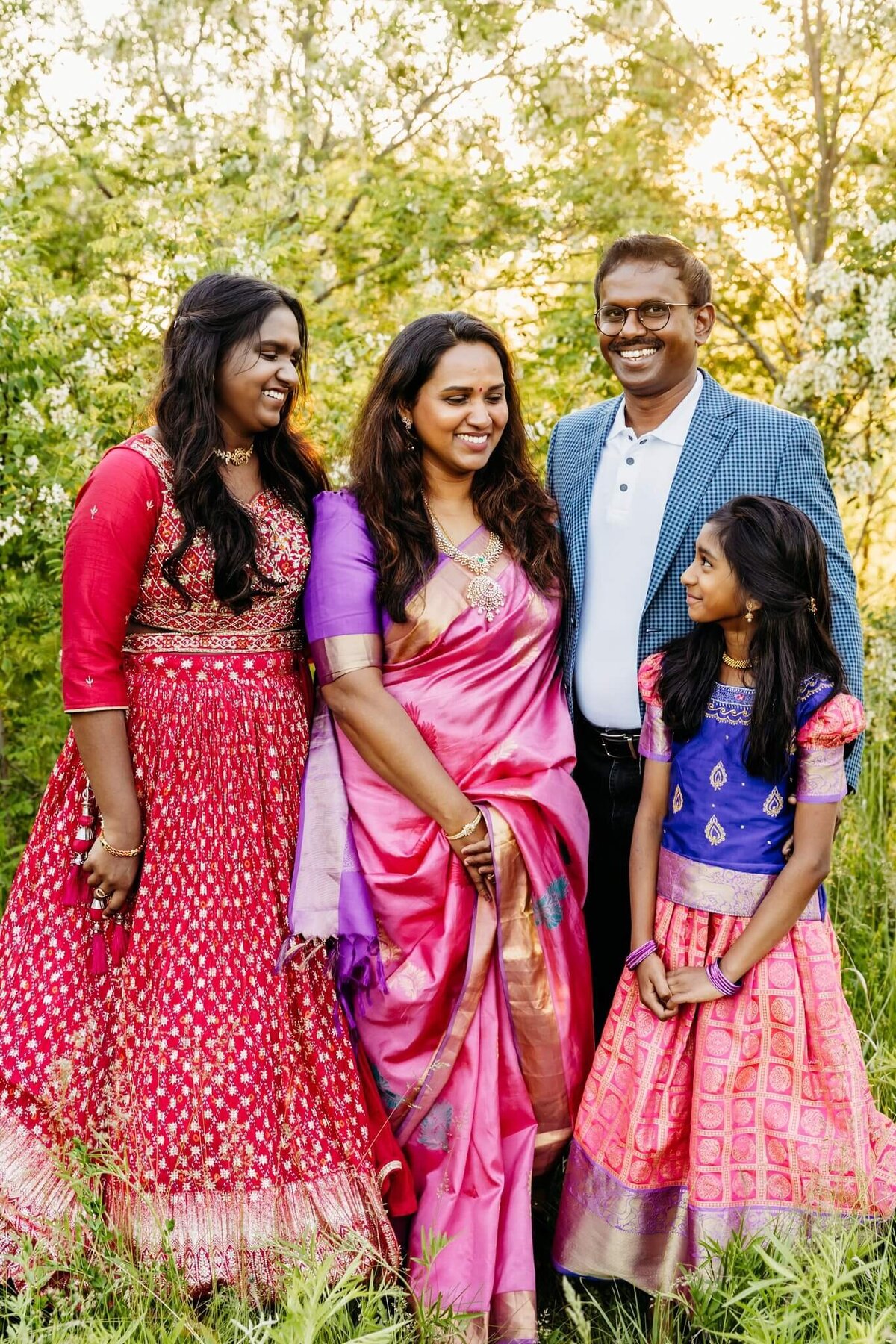 Mom and dad stand next to their two daughters and they look at each other and laugh in a park near Milwaukee.