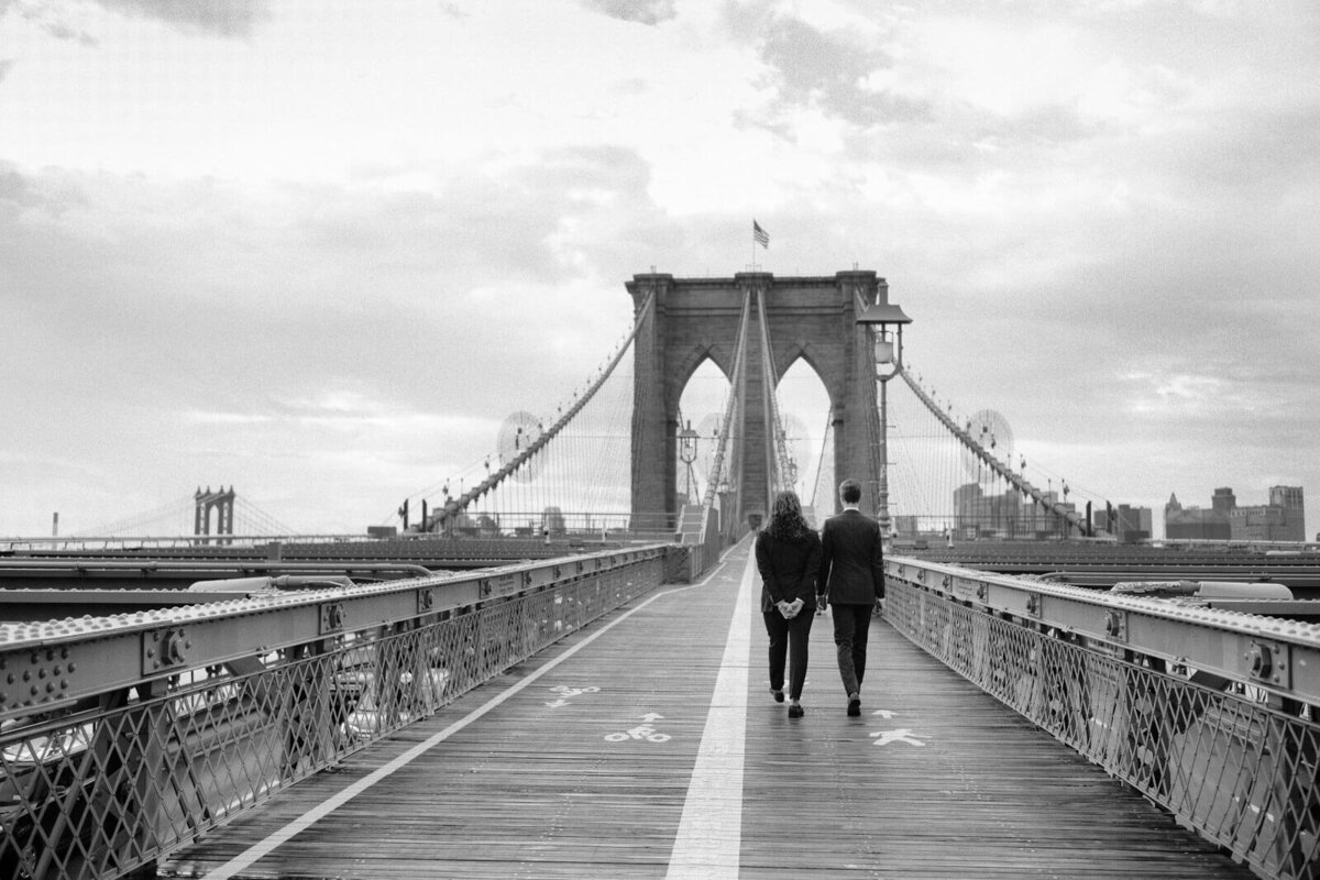The two grooms are walking on the Brooklyn Bridge. NYC City Hall Elopement Image by Jenny Fu Studio