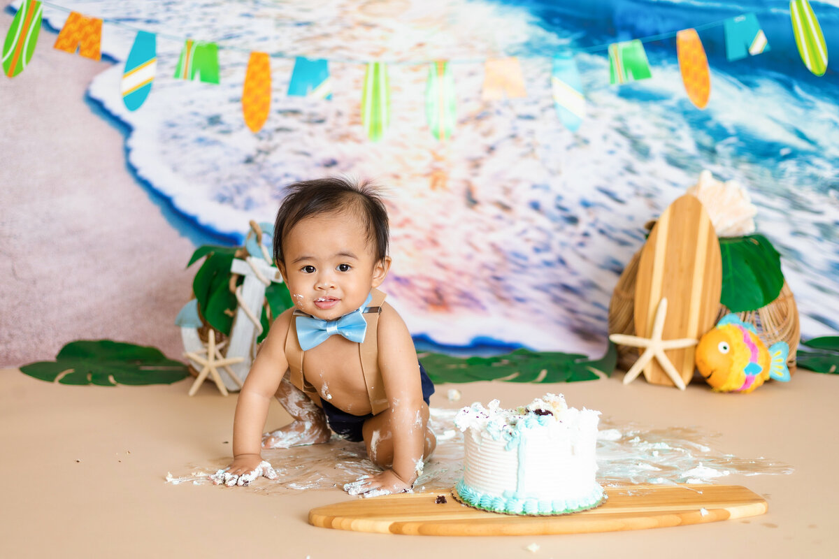 Cake Smash Photographer,  a baby boy is covered in cake during surf-themed first birthday