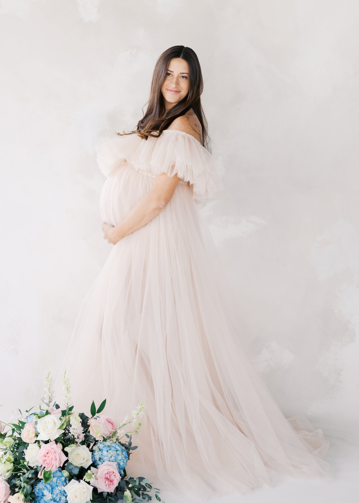 Beautiful woman in tulle maternity gown holds her belly for her minneapolis studio maternity session with angela watts photography.