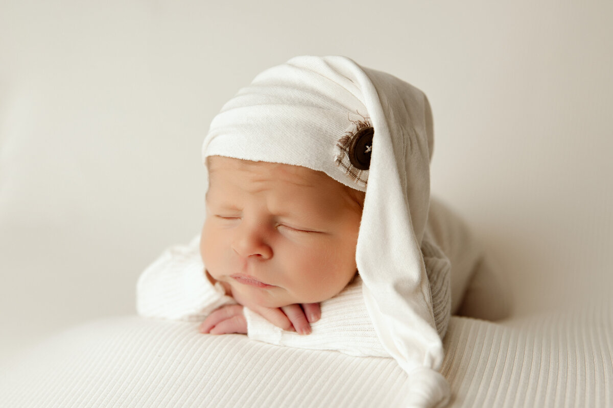 newborn boy in chin on hands pose wearing a white stocking cap