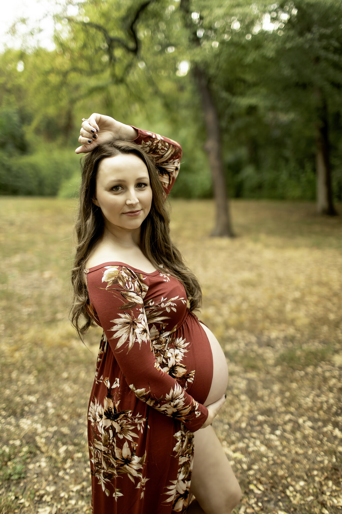 A vibrant maternity photo of the expectant mom in a red dress, standing confidently on a park path at Trinity Park, with sunlight filtering through the trees, captured by Chunky Monkey Photography.