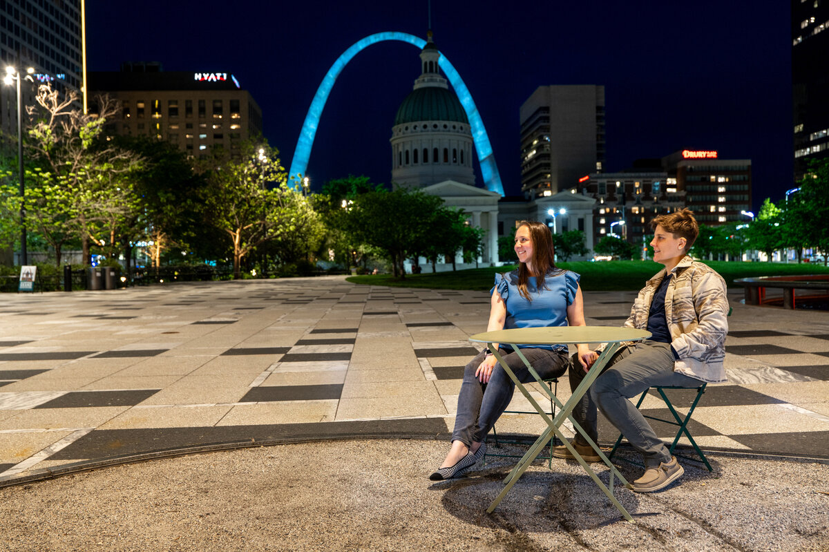 A couple sitting at a small table outside smiling 