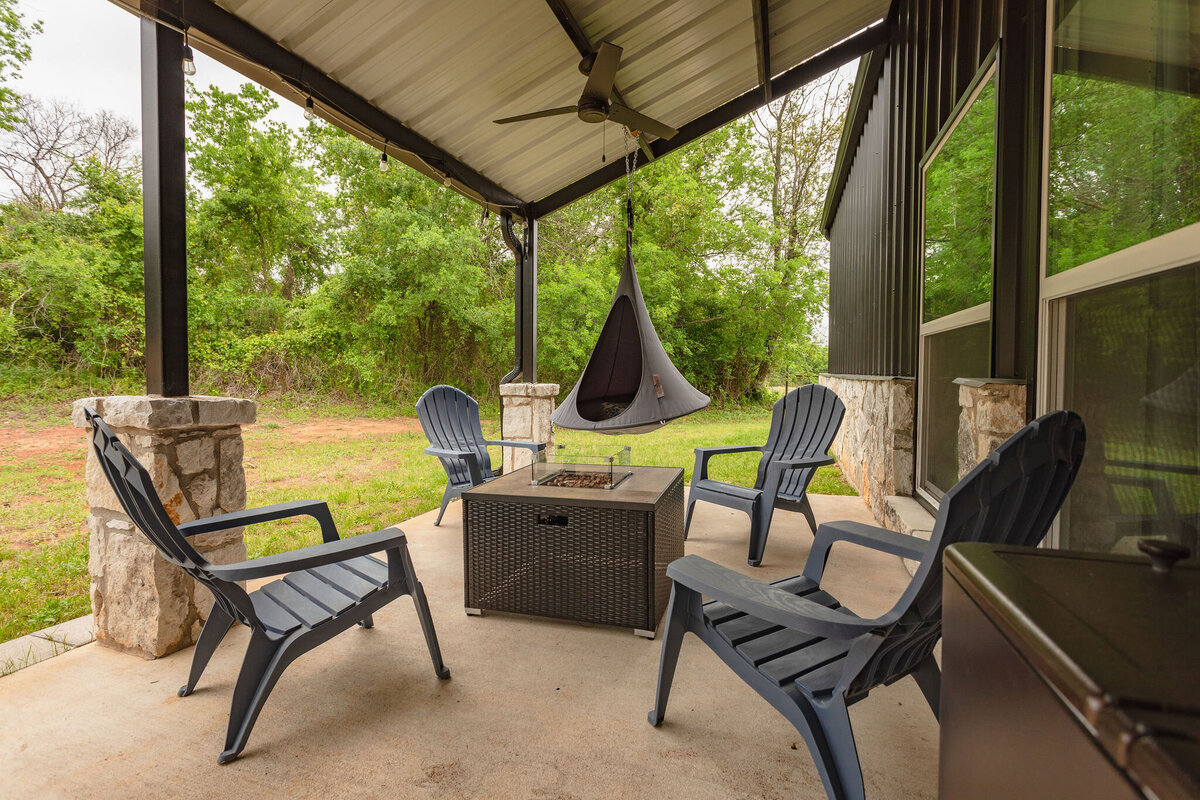 Covered patio with firepit and plenty of seating at this five-bedroom, 3-bathroom vacation rental house for up to 10 guests with free wifi, private parking, outdoor games and seating, and bbq grill on 2 acres of land near Waco, TX.