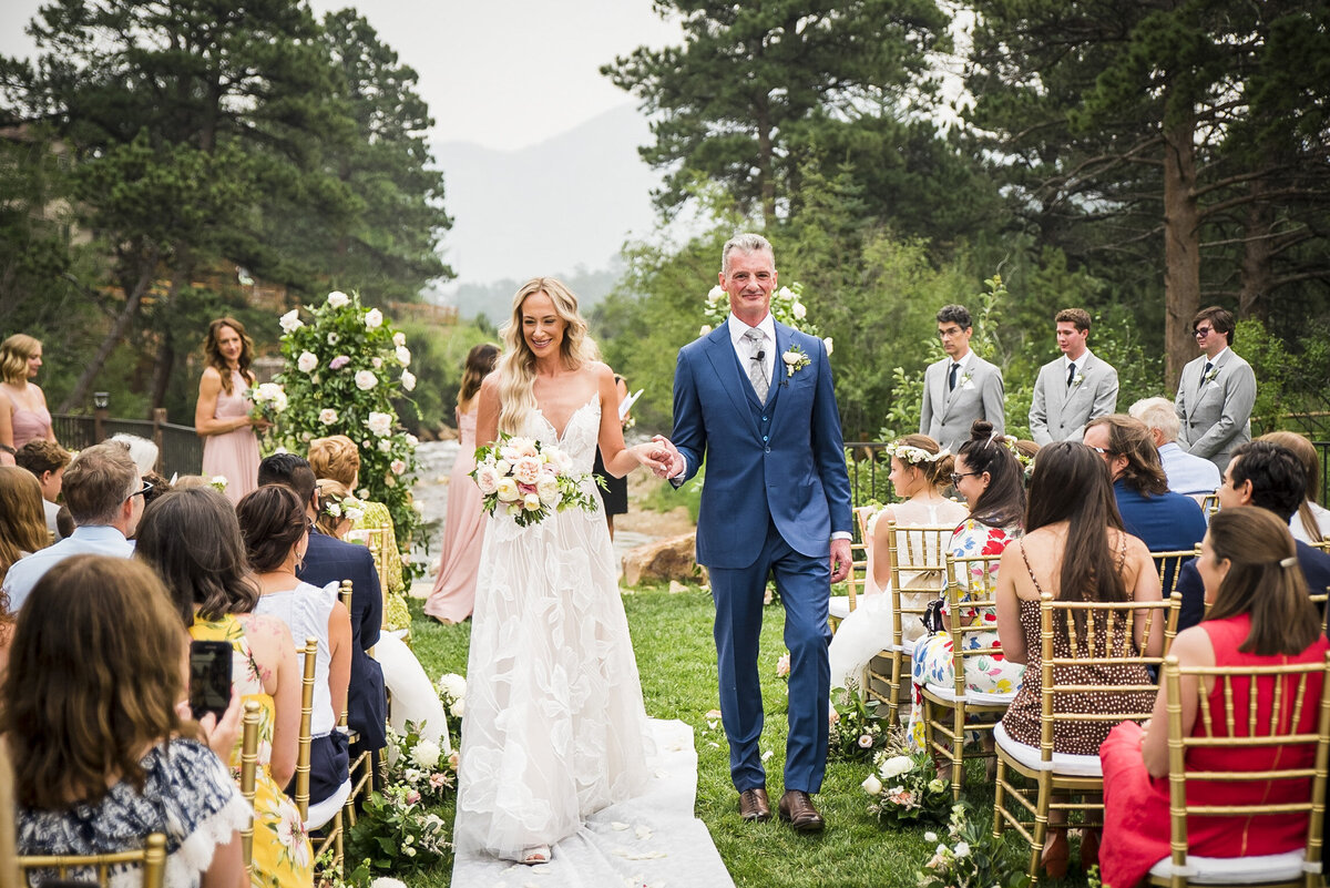 A bride and groom walk back up the aisle at the end of their ceremony, smiling at their guests.