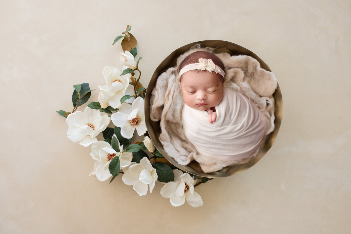 baby girl sleeping in a basket surrounded by magnolia flowers