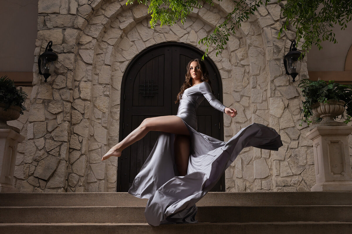 A senior girl twirls on stone steps, styled for senior photos Dallas with dramatic lighting.