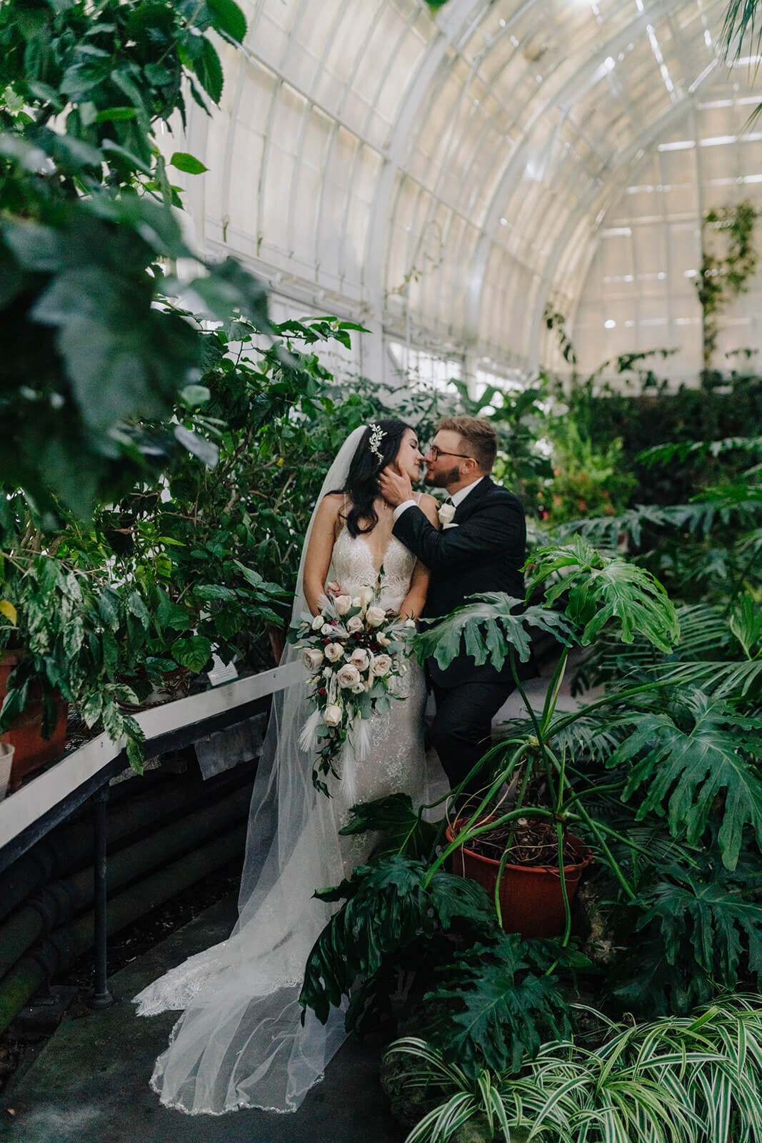 Bride and groom kissing amongst green foliage