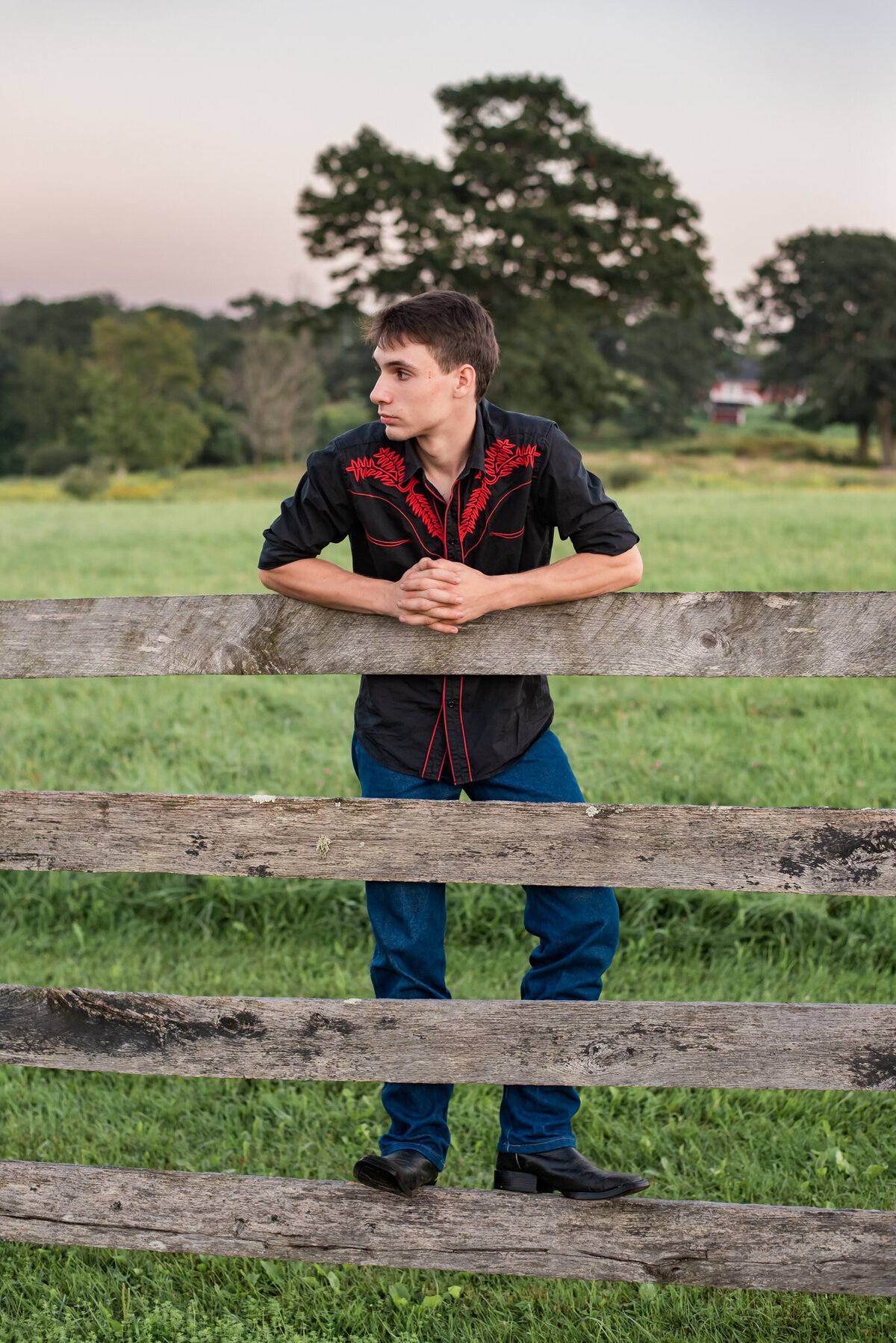 Senior boy looking off camera and leaning on fence at sunset