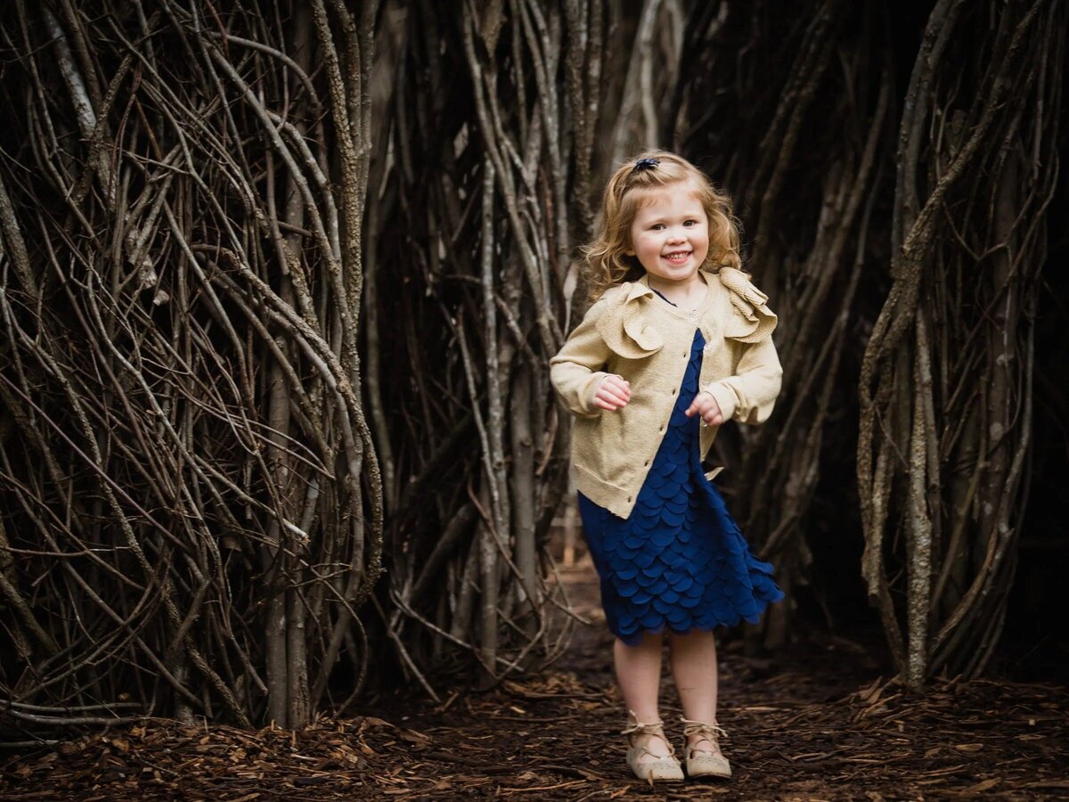 A small girl standing in a wooded area.