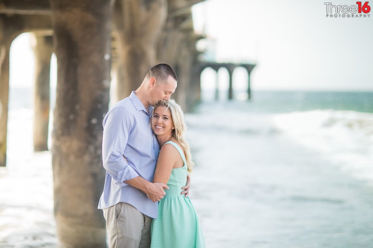 Groom to be kisses the top of his Bride's head during photo shoot at the Manhattan Beach Pier