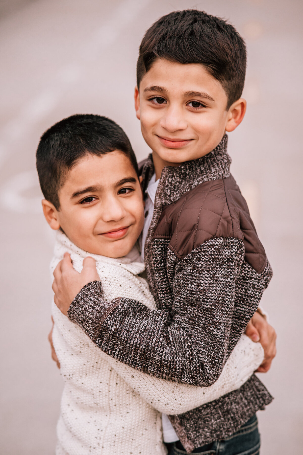 Two young boys hugging each other, smiling warmly at the camera.