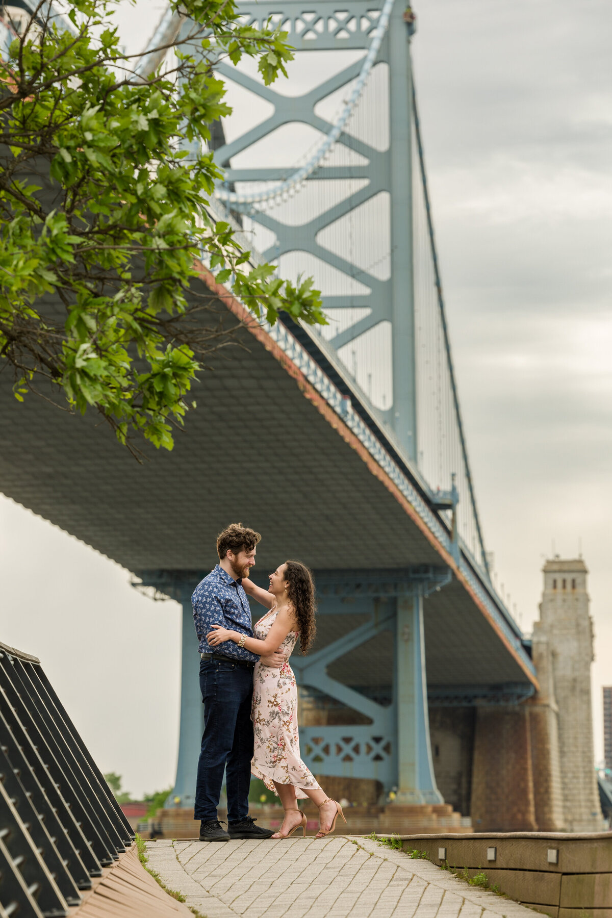 An engaged couple enjoying a romantic moment at Race Street Pier in Philadelphia during their engagement session, with the iconic city skyline providing a stunning and scenic backdrop for their photos.