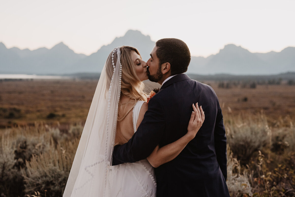 Photographers Jackson Hole capture bride and groom kissing in front of Tetons