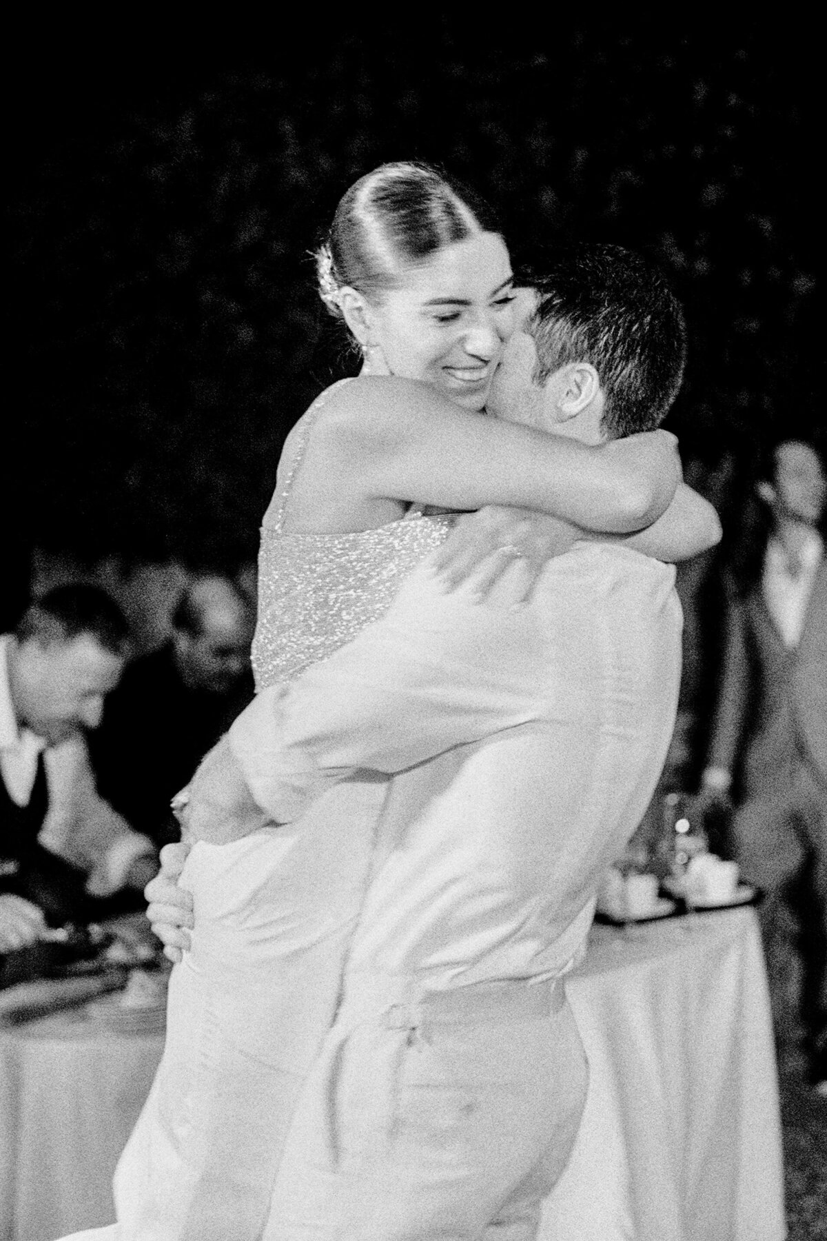 Black and white photograph of bride jumping on and hugging her groom at their wedding reception photographed by Italy wedding photographer at Villa Montanare Tuscany wedding