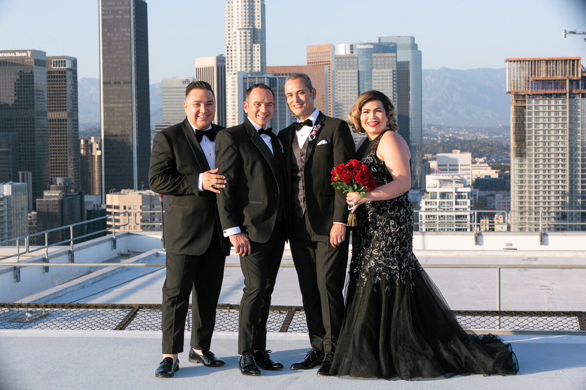 Grooms standing with two wedding guests on a city rooftop