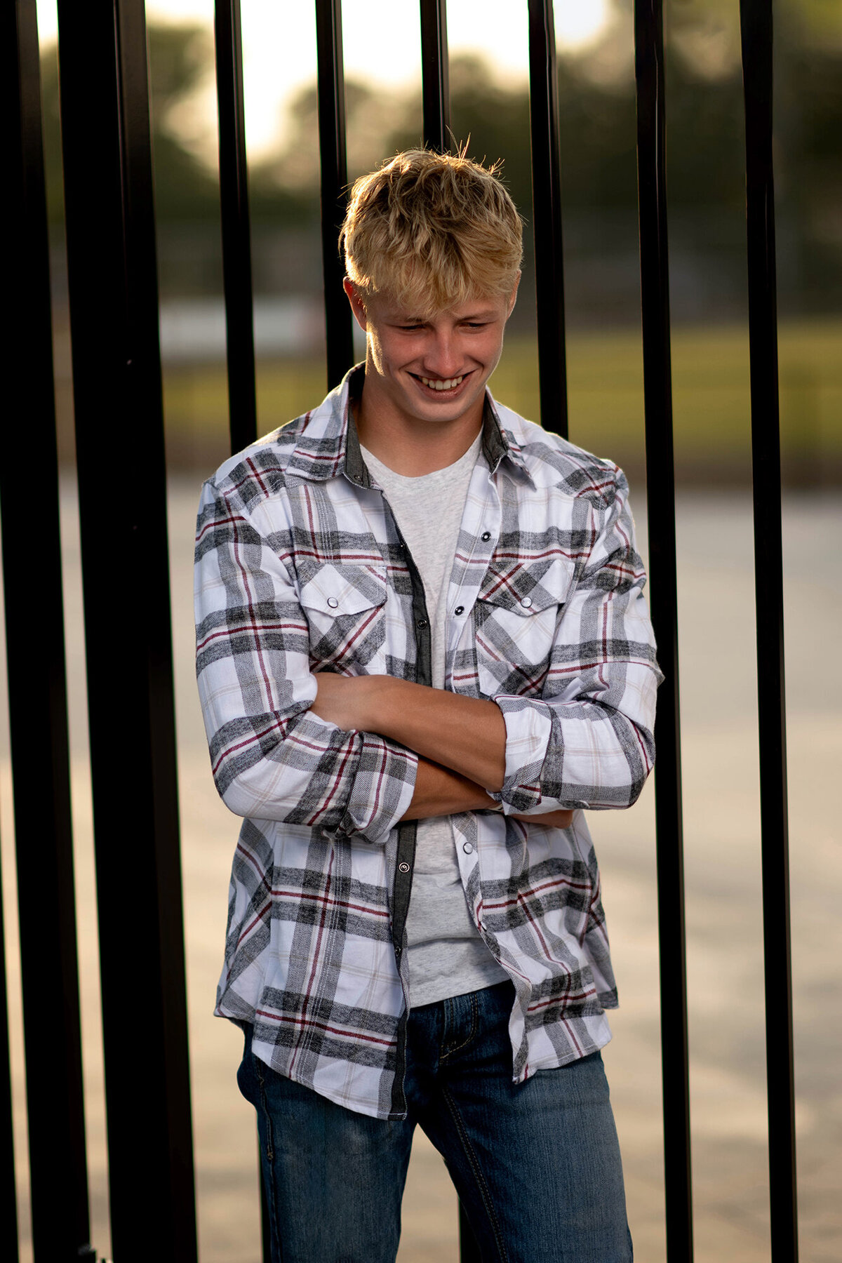 A high school senior in a plaid shirt leans on a metal gate while laughing